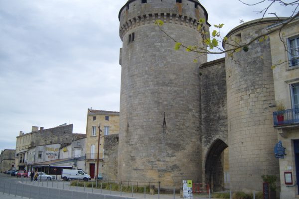 A stone-built gateway flanked by two round towers. A road runs in front of the gateway.