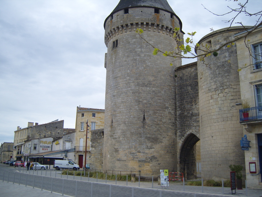 A stone-built gateway flanked by two round towers. A road runs in front of the gateway.